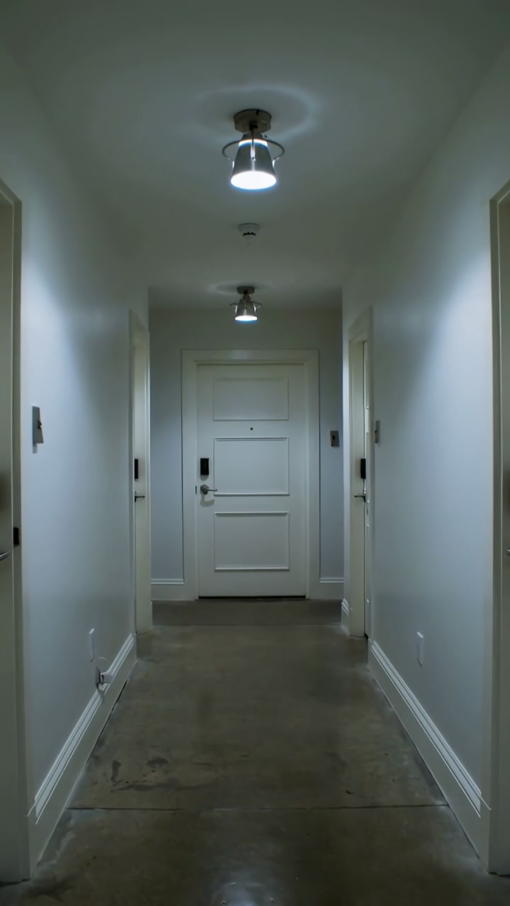 Vertical video: Moving camera down narrow hallway toward white end door, showing electronic lock