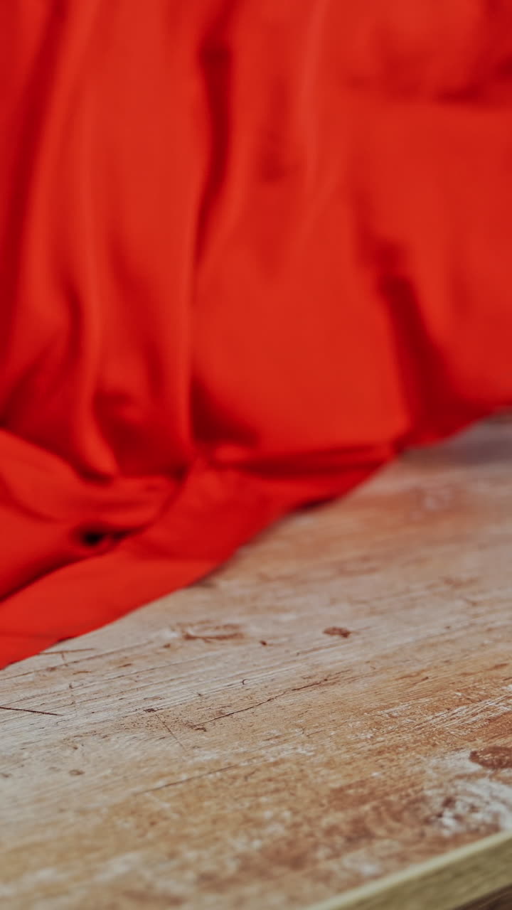 Seamstress laying out beautiful red cloth on a wooden table. Work place table of tailor in workshop and a big piece of red fabric indoors. Vertical video