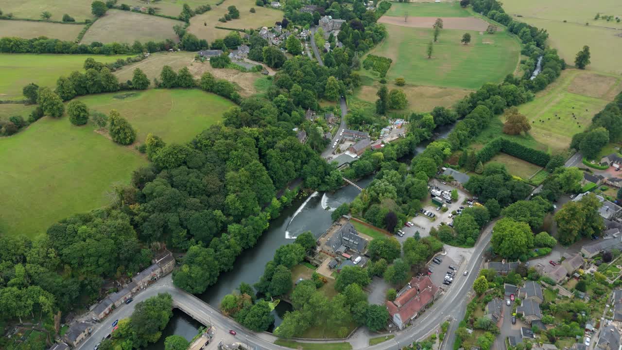 Drone video showing countryside river and small town nestled in green valley, Derbyshire Dales, United Kingdom