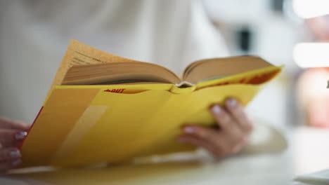 close-up of an open yellow book with soft-focus background and hands holding pages, emphasizing reading and learning in a quiet, serene environment