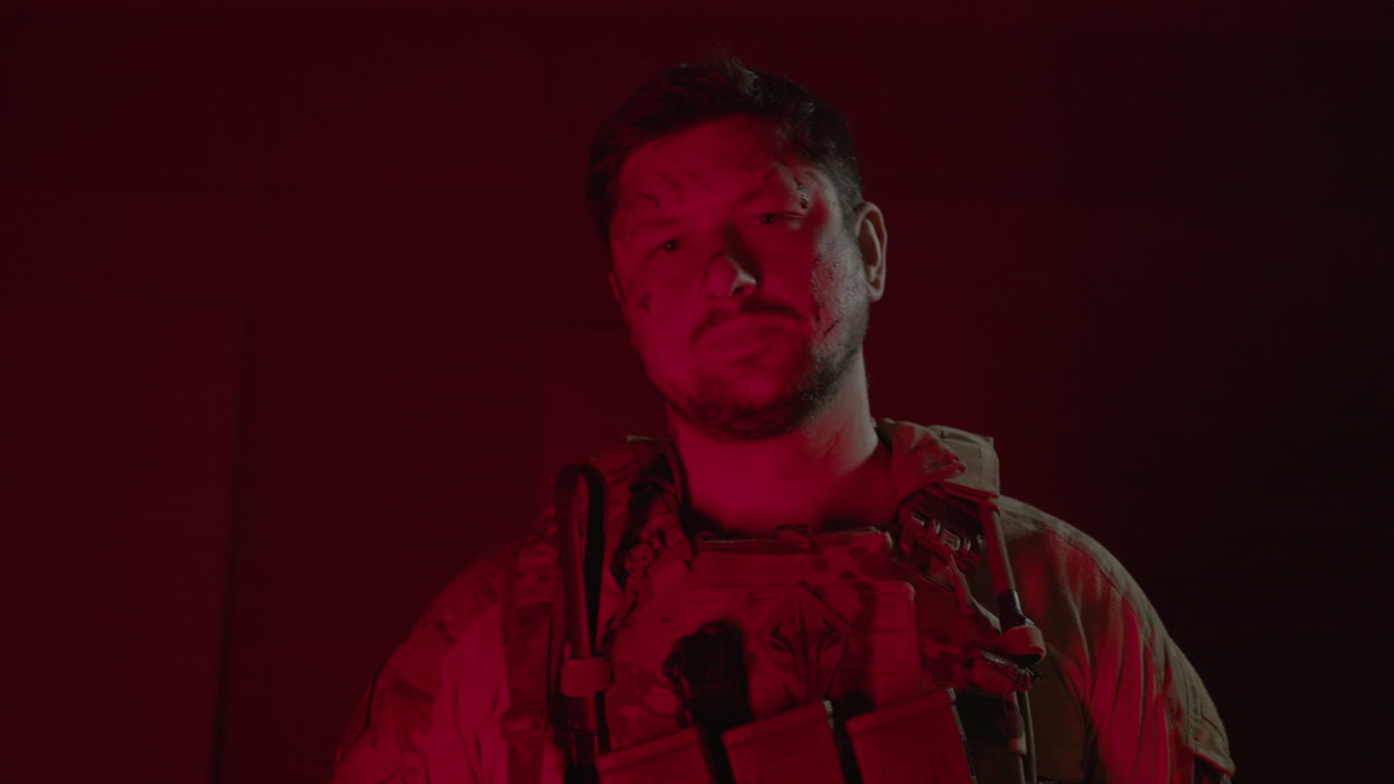 一名持有猎枪的男子在玩软球后,在黑暗房间里摆姿势,闪闪发光的红光