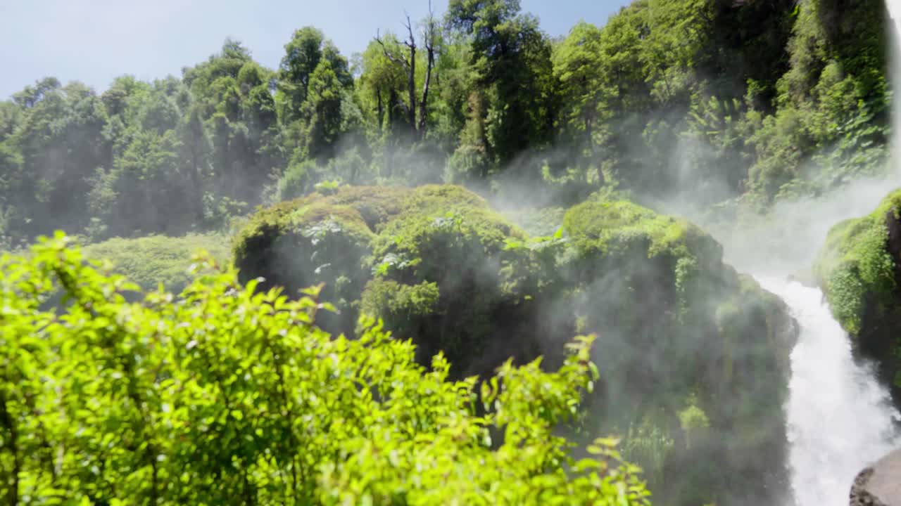 Pan left of Salto El Leon misty waterfall streaming over rocks covered with moss in green forest near Pucon, Chile