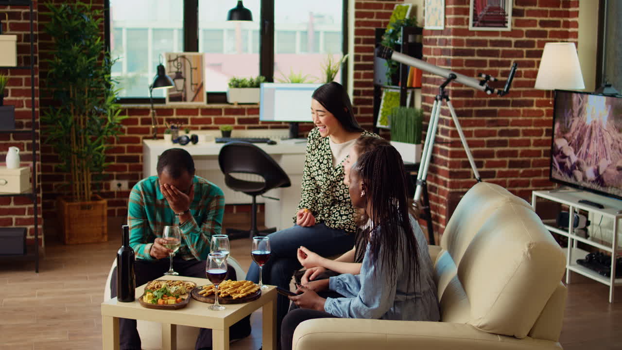 Multiethnic friends looking at funny videos on smartphone screen, laughing while drinking wine