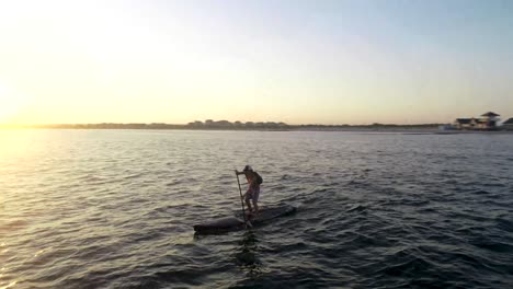 paddleboarder paddling away into the sunset.