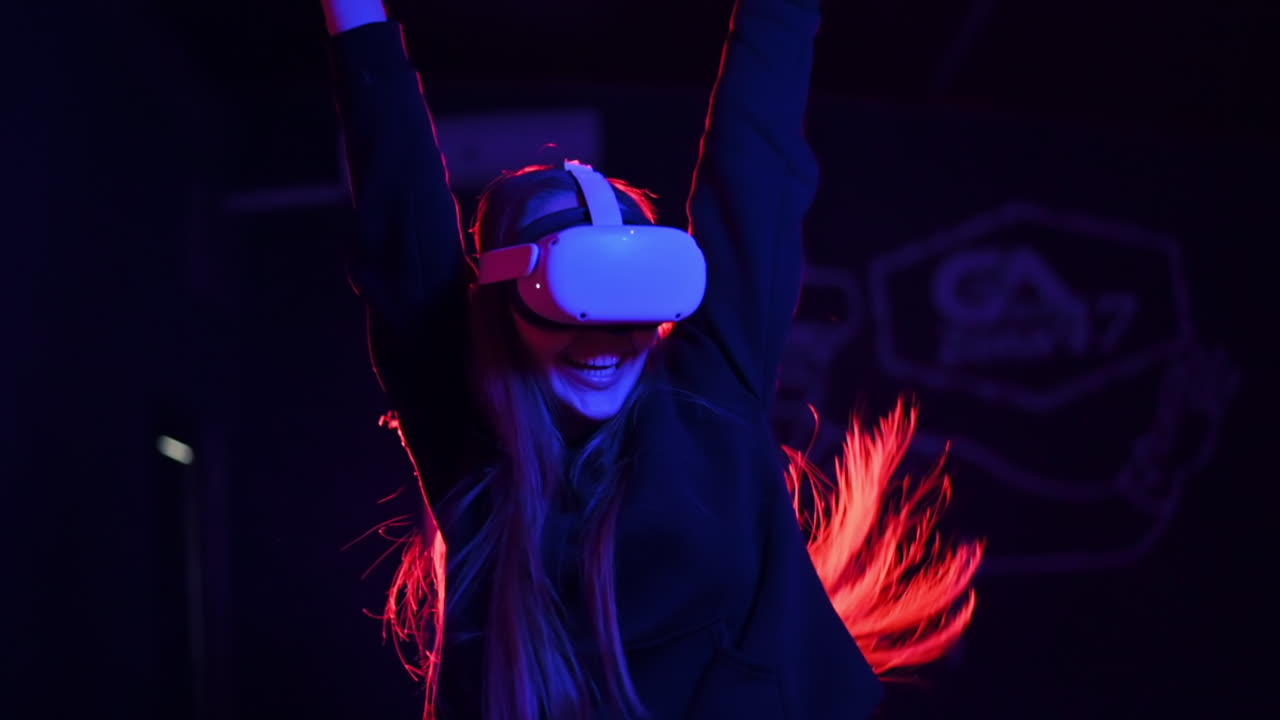 A young woman is happy about winning the VR game using VR glasses and controllers. Red and blue illumination. Slow motion