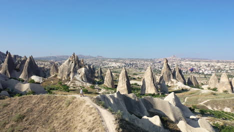 Epic-revealing-drone-shot-of-a-lone-man-standing-on-top-of-a-hill-while-the-fairy-chimneys-behind-him-in-Cappadocia,-Turkey