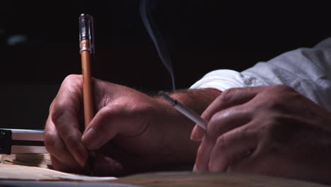 a man in lamplight, smoking a cigarette, processing information from a dictaphone and taking notes on paper