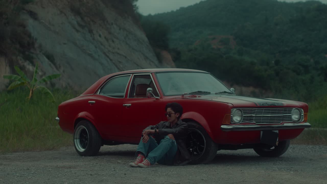 Man sitting by vintage red car in nature