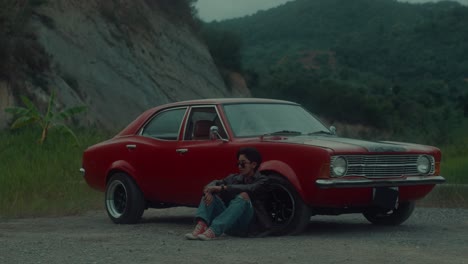 man sitting by vintage red car in nature
