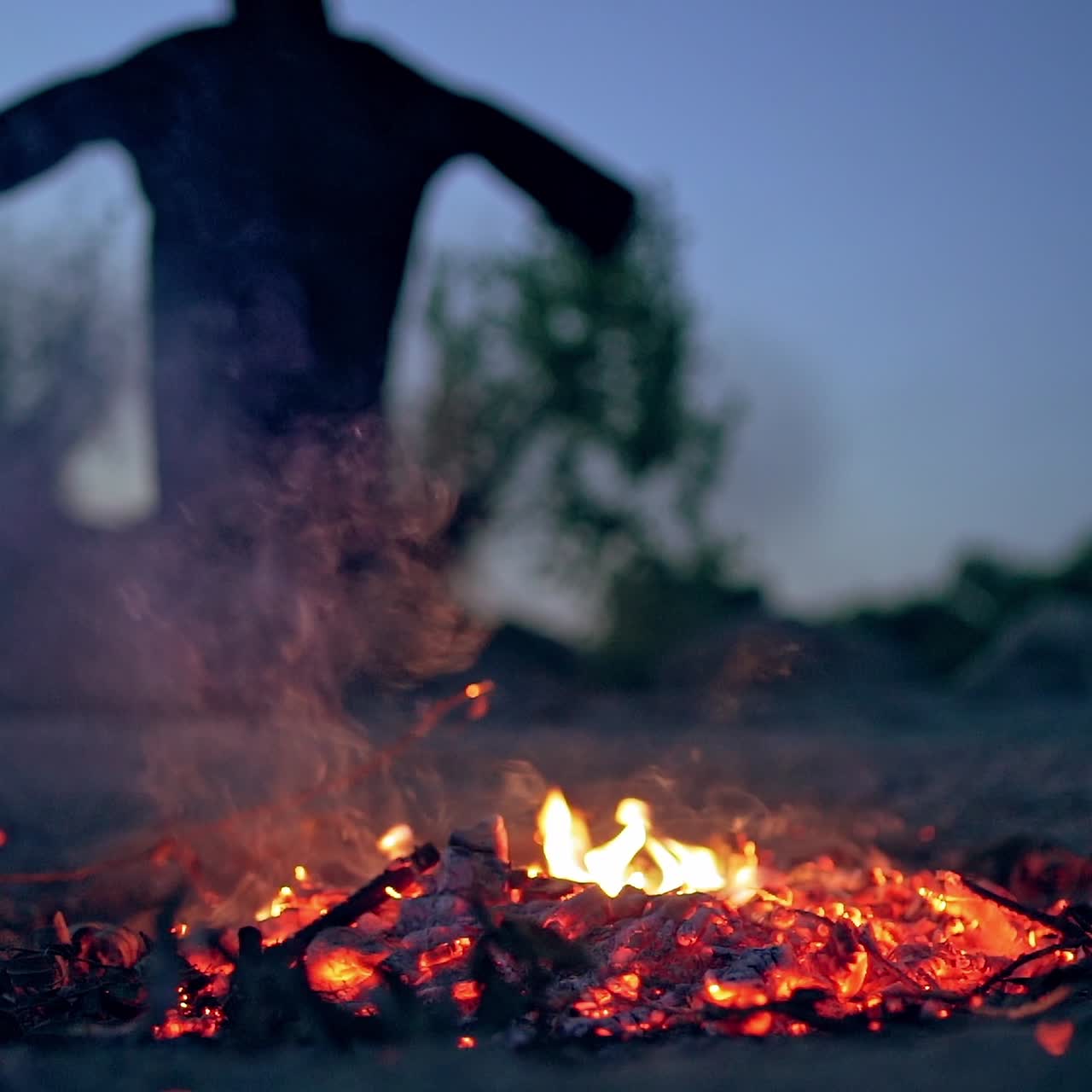 Embers of fire and scary witch outdoors. Death in black costume goes away from fire. Halloween concept.