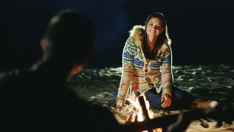 man playing guitar to his girlfriend sit around the campfire in the evening next to each other