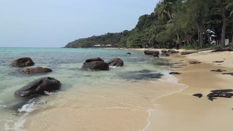 Static-seascape-shot-of-a-white-sand-beach-and-the-ocean-on-a-tropical-island-of-Koh-Kood-in-Thailand-with-waves-hitting-the-rocks-and-shore