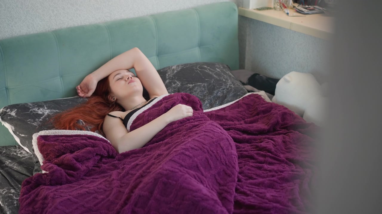 Ung dame sover bag sløret døråbning. Søvnig kvinde ligger ubemærket på sengen med mystisk stemning. Ung kvinde hviler stille på sengen bag uklar døråbning med gådefuld atmosfære.