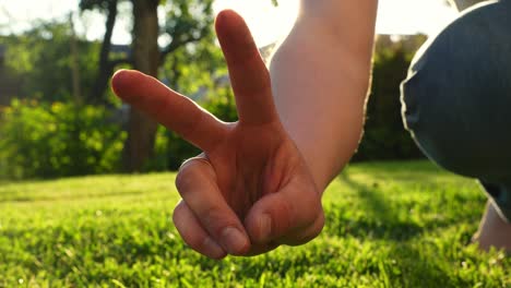 close up of person making peace sign with fingers with garden background at sunset