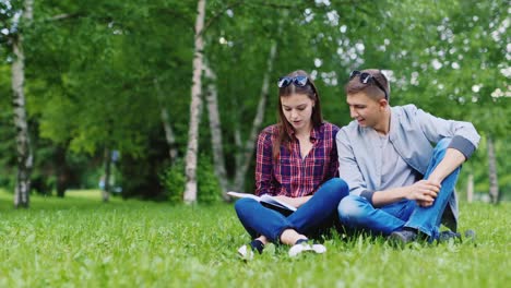 young man and woman sitting on grass looking at book