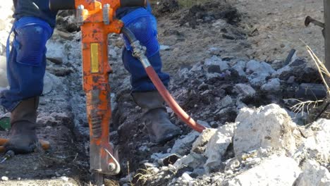 man clearing debris with shovel in trench by his jack hammer close up camera