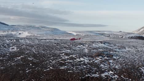 red helicopter parked on rugged snowy hill in winter landscape of iceland