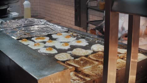 Cooking-fried-eggs-and-toast-on-a-hot-plate-griddle-in-a-restaurant-kitchen-at-breakfast