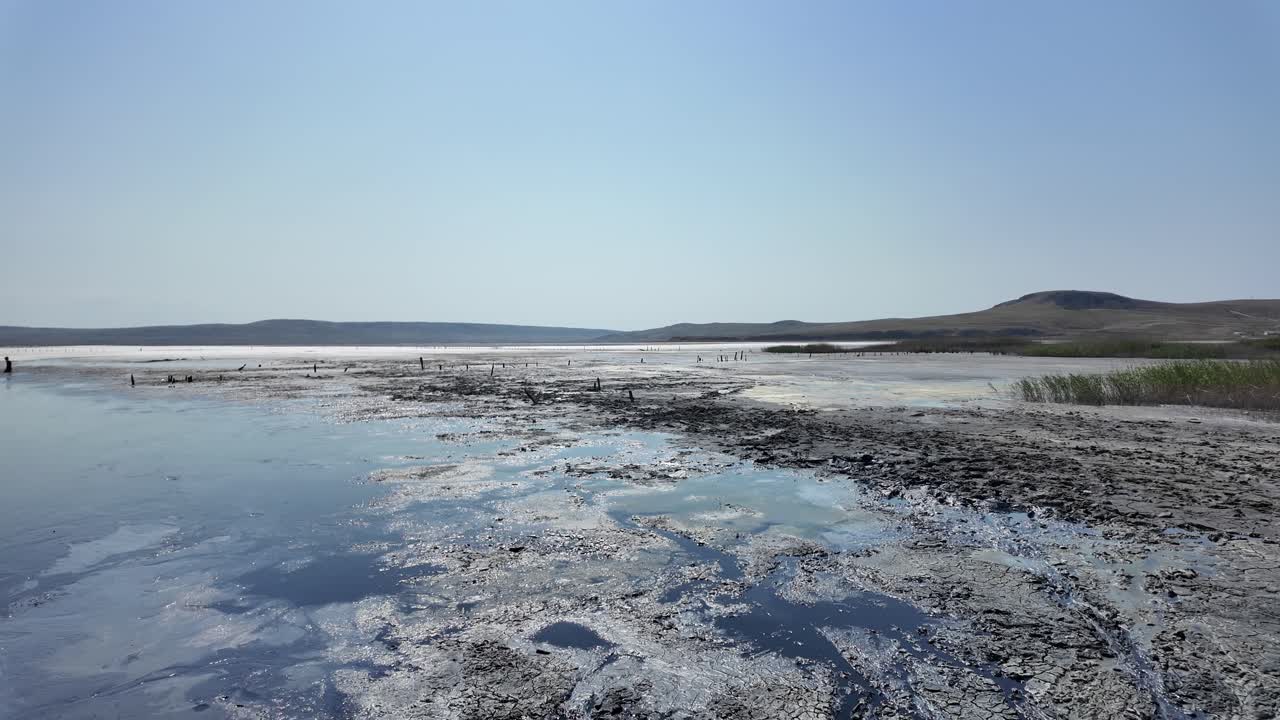 A vast, desolate lake with muddy, discolored water and distant hills under a clear sky
