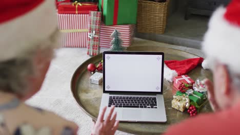 Caucasian-senior-couple-in-santa-hats-on-video-call-on-laptop-with-copy-space-at-christmas-time