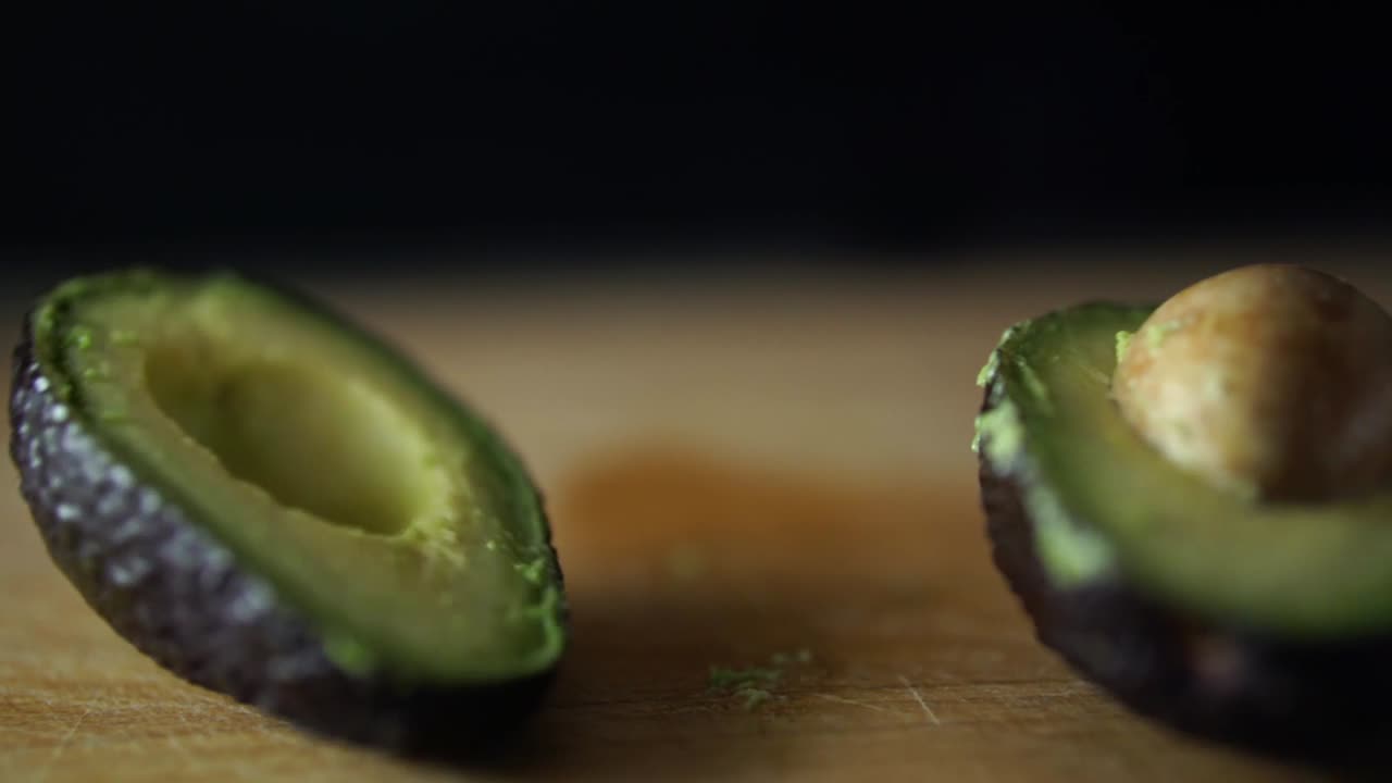 dita del maschio caucasico rilasciando avocado dimezzato che viene diviso aperto sul tagliere di legno, rallentatore