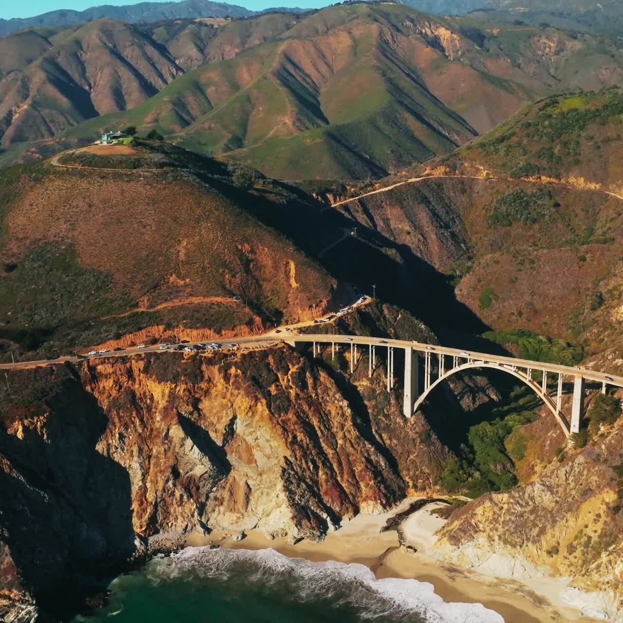 Majestic rocks at the coast of California, USA. Arched bridge connecting the highways on the mountains. Sunny day footage