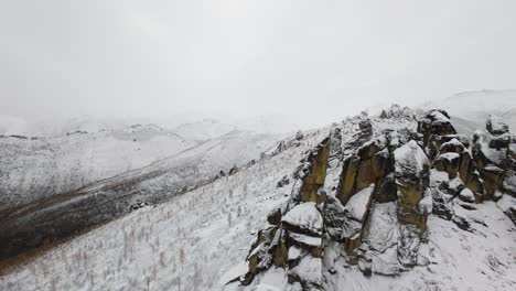 Experience the serene beauty of towering mountains blanketed in snow as a drone glides above the majestic peaks and valleys during a tranquil winter morning