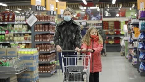 mom and daughter, shoppers in the mall, walk between the shelves with goods and roll a shopping cart in front of them.