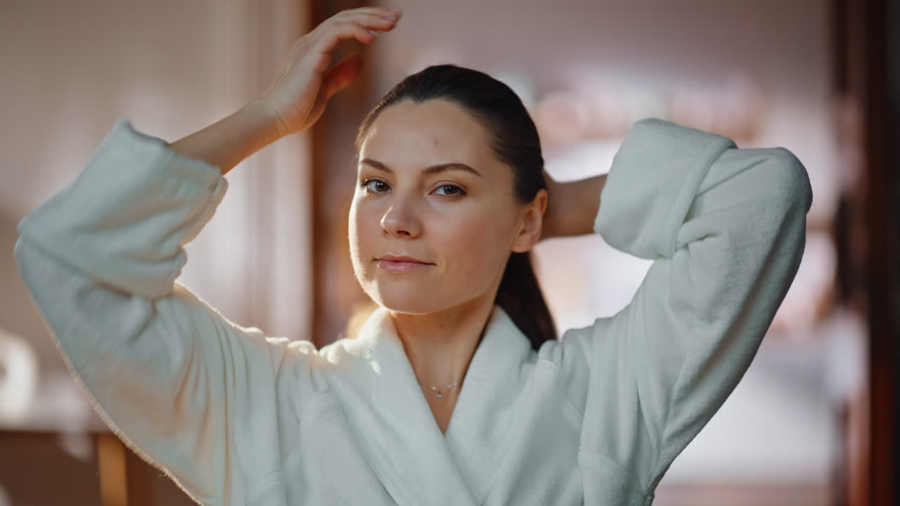 Home woman making ponytail looking mirror wearing robe closeup. Relaxed lady