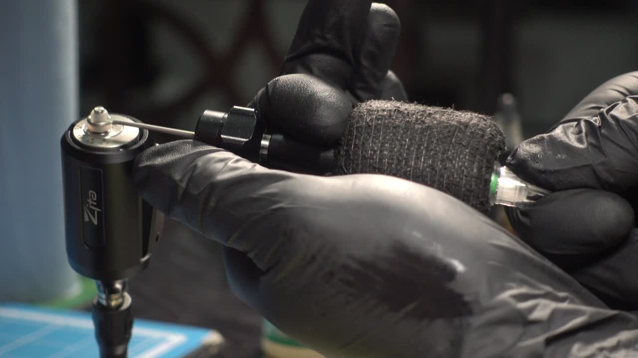 татуировщик загружает татуировочную машину иглами