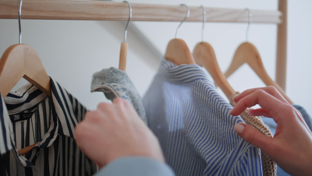 Woman hands flipping hangers choosing clothing at large wardrobe closet closeup