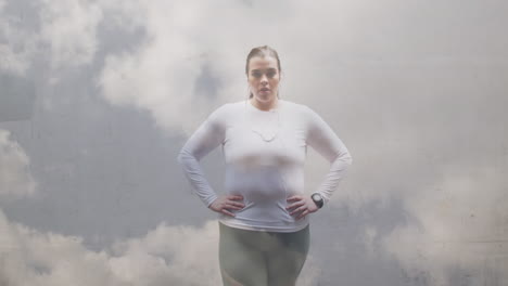 animación de nubes sobre tamaño grande mujer caucásica en ropa deportiva flexionando los músculos