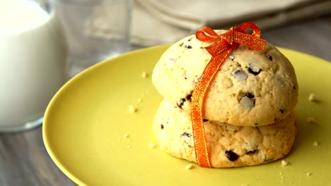 deliciosas galletas de patatas fritas de chocolate dulce con una cinta de naranja. jarro de leche en una mesa de madera. en bucle