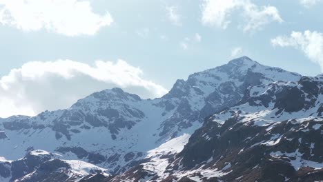 snow capped pizzo tambo dominates the landscape near montespluga, italy, under a bright blue sky dotted with white clouds