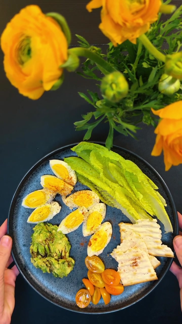Mani che tengono un piatto di cibo sano per la colazione. Primo piano, vista dall'alto di mani che tengono un piatto blu con uova, avocado, pomodori e cracker.