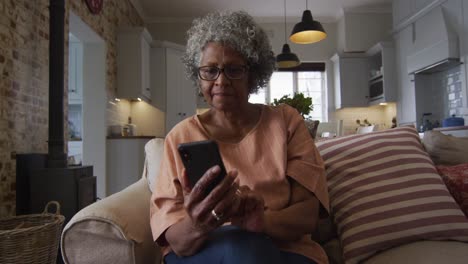 Ältere-Afroamerikanische-Frau,-Die-Ihr-Smartphone-Benutzt,-Während-Sie-Kaffee-Trinkt,-Während-Sie-Auf-Der-Couch-Sitzt