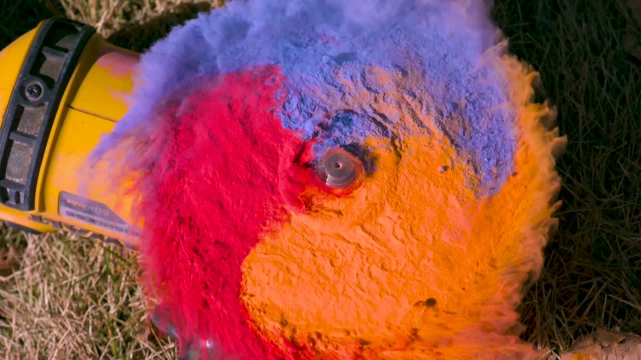molino de ángulo o un molino de disco que tiene polvo de tiza naranja, rojo y azul en él comienza a girar y salpica el polvo en una nube en cámara lenta