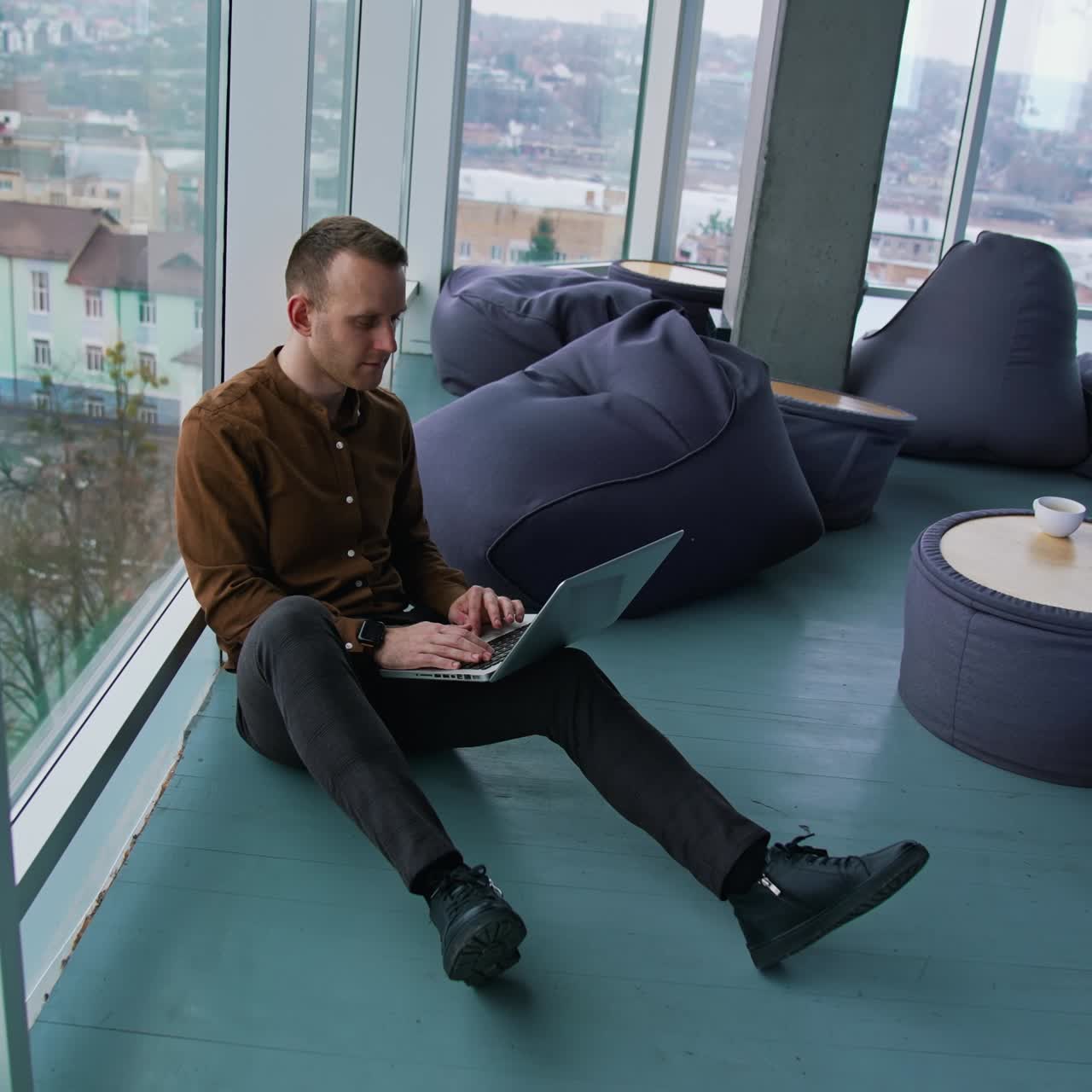 Young man with laptop sitting on floor by the window