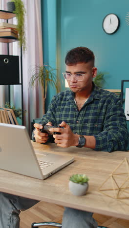 excited indian man playing video game on laptop computer spending leisure time at home office