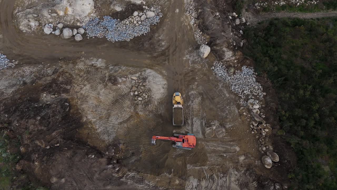 aerial view of excavator working with dump truck at rocky dirt worksite