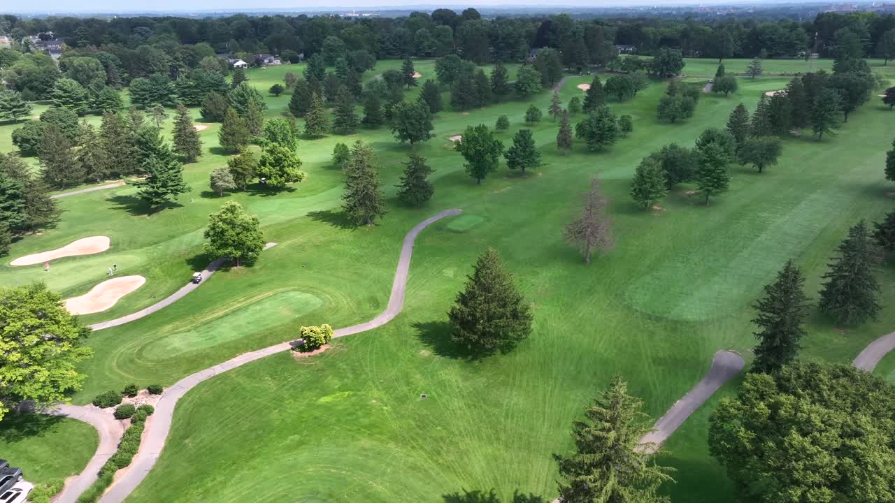 Slow drone flight over green golf course on hill with sand bunker and golf cart. Wide shot. Green fir trees and plants in summer. Quiet and peaceful nature of USA