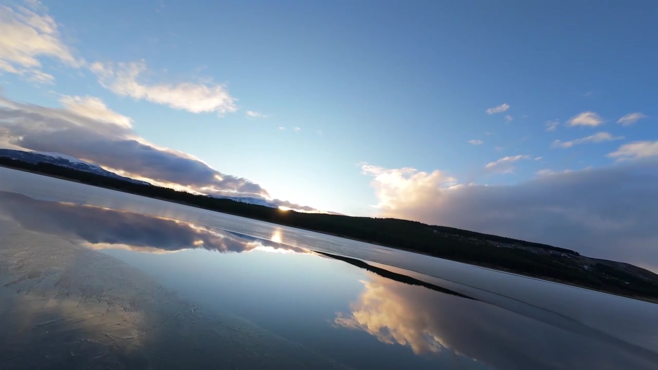 Cinematic FPV drone flight skimming the calm, mirror-like waters of Laguna La Zeta in Esquel, Argentina, perfectly reflecting the stunning sunset clouds.