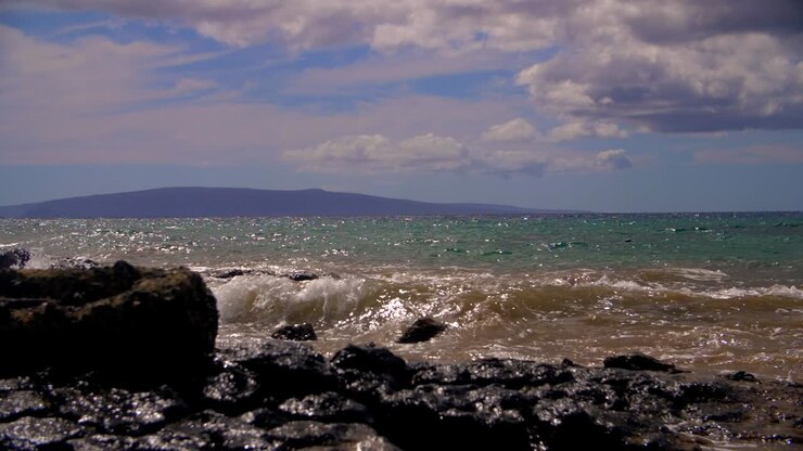 Costa sabbiosa delle Hawaii con roccia, montagna in lontananza e snorkeler in slow motion