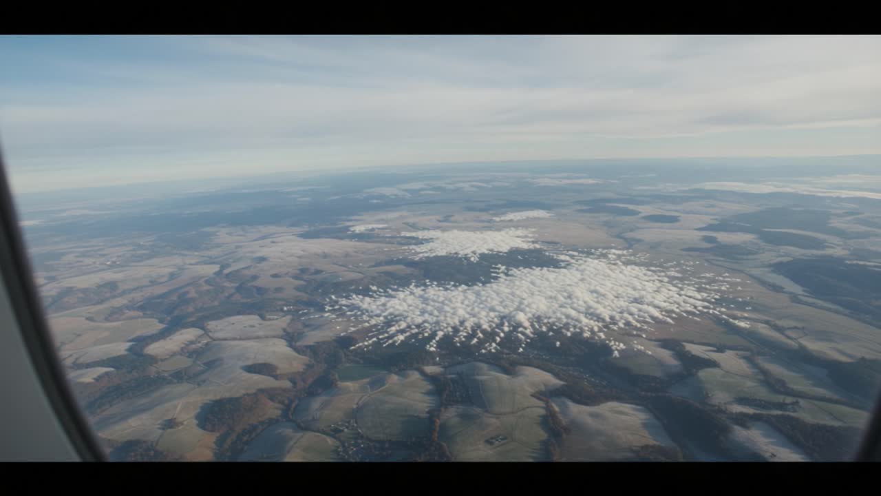 Luftfoto, der fanger store landskaber med skymønstre, der ruller hen over fredfyldt terræn, som set gennem et flyvindue på en klar dag