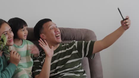 happy asian family using phones, sit at home on the couch and communicate via video call