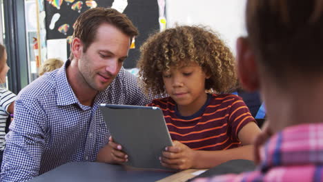 Teacher-and-young-schoolboy-using-tablet-computer-in-class