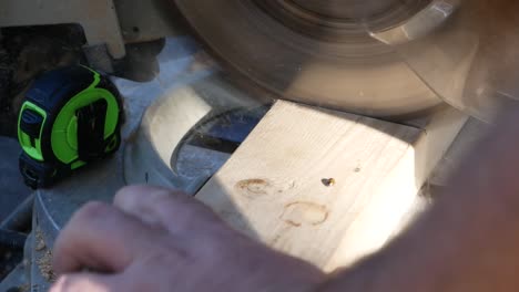 male carpenter using a sharp circular saw to cut through a piece of wood, close up