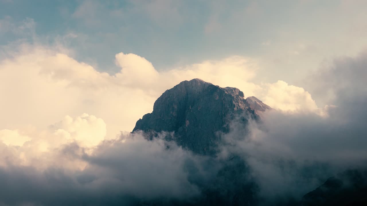 Cima di montagna che emerge attraverso nuvole dense e nebbia dorata con la luce del sole che illumina il terreno accidentato, paesaggio naturale drammatico con atmosfera suggestiva e luce soffusa
