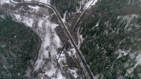 vista aérea de los coches circulando por una carretera rural de invierno en un bosque nevado.