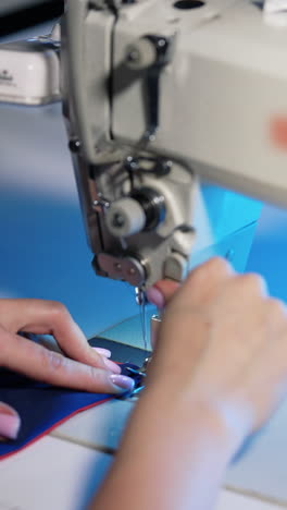 woman works at sewing machine. female hands moving cloth while needle of the sewing machine doing stitches in atelier. vertical video